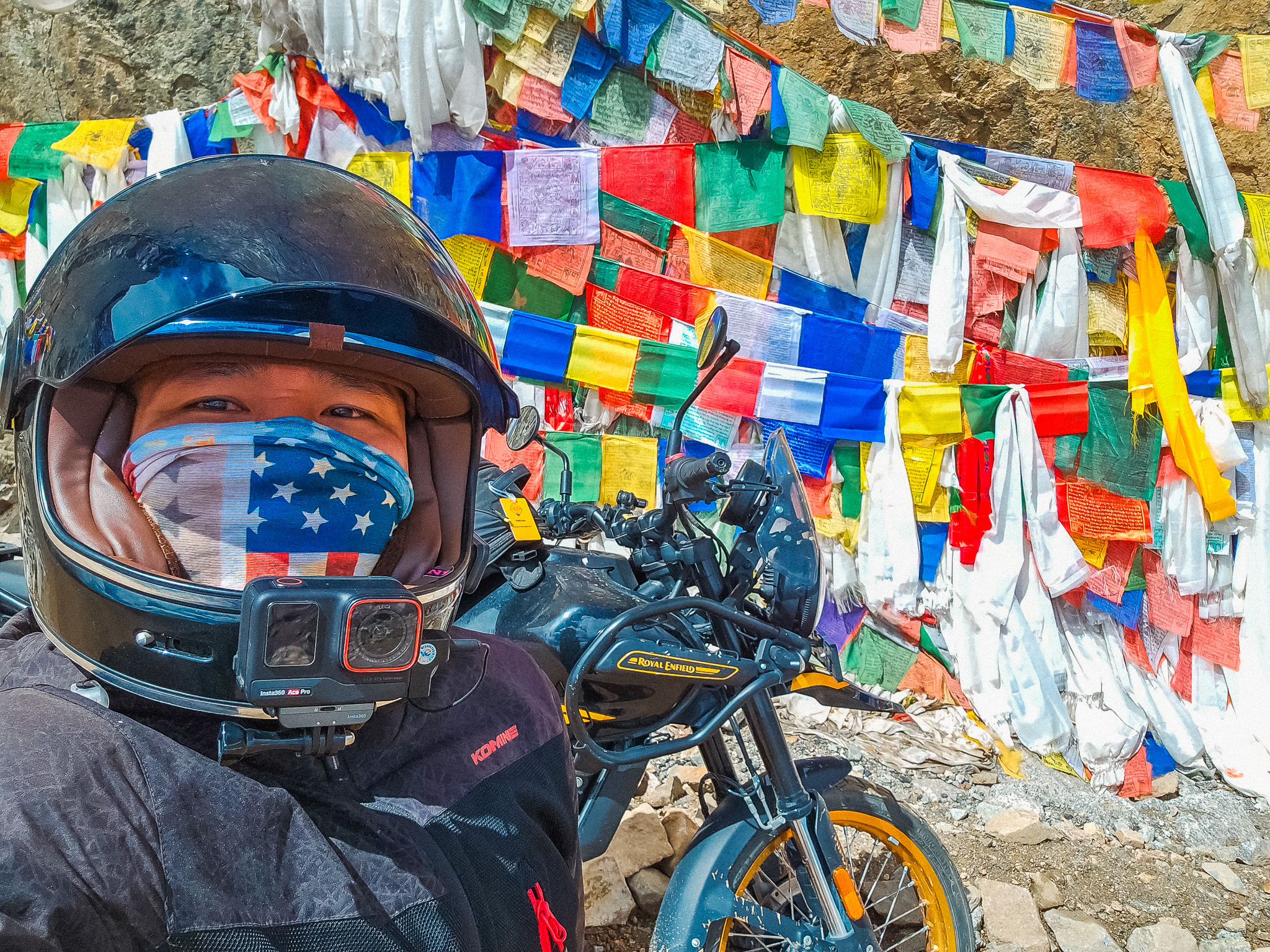 A motorcycle rider poses with the Indian flag against a backdrop of majestic mountains