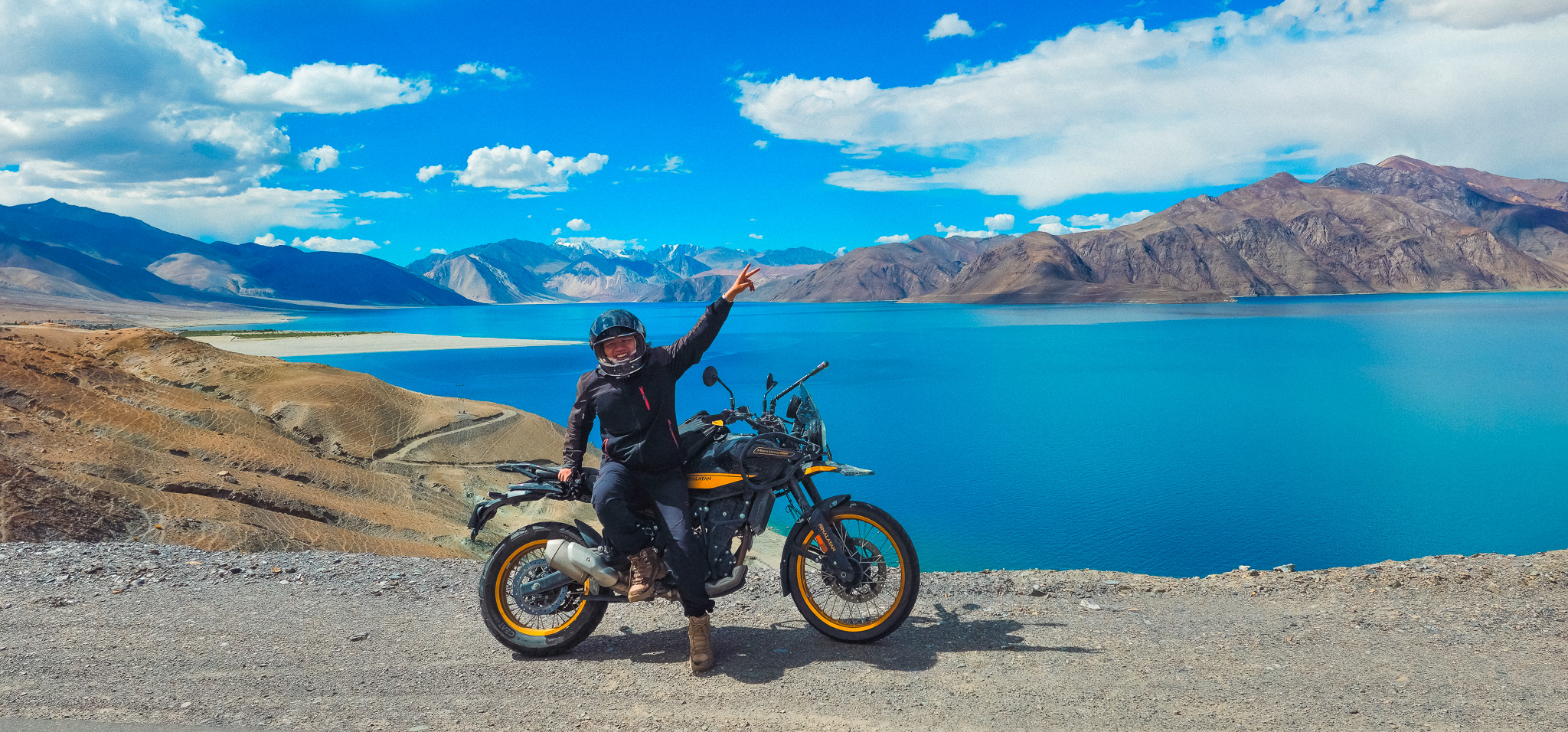 A motorcycle rider takes a break amidst a stunning mountain range