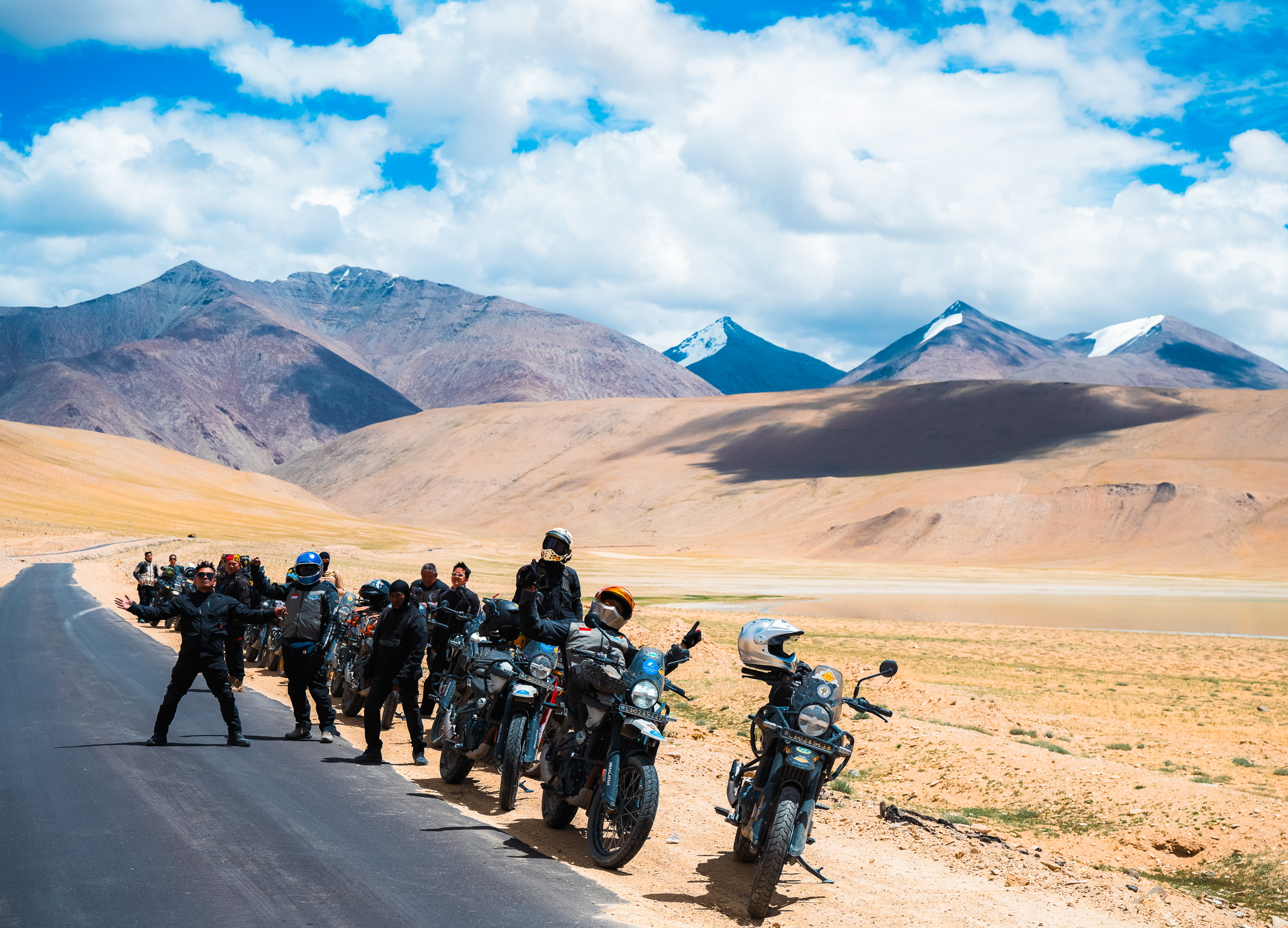 A group of motorcycle riders pose on a winding road with a vast landscape in the background