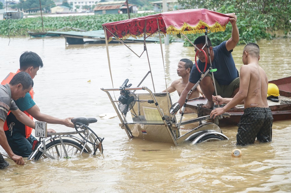 Khu vực này vốn là bãi đỗ xe, nhưng chỉ sau một đêm, nước sông Hồng đã dâng lên nhấn chìm mọi thứ. Anh chủ xích lô phải lặn ngụp mãi, hơn một giờ mới kéo được phương tiện kiếm cơm lên chỗ cao hơn.