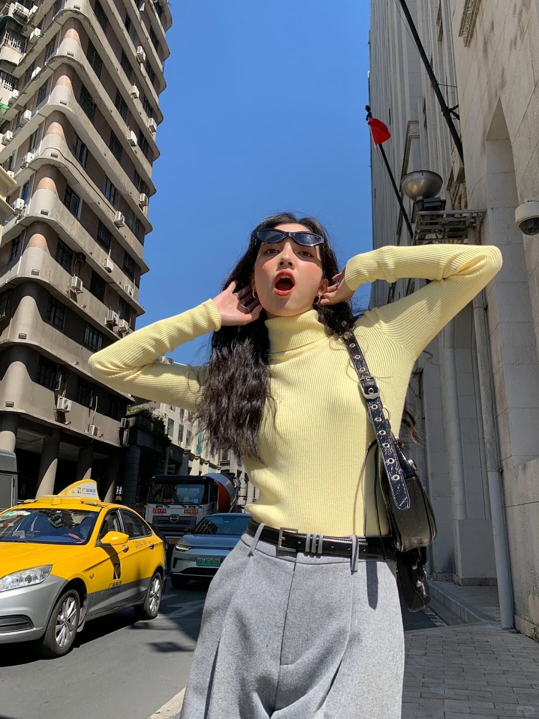 A woman wearing a beige turtleneck sweater, white pants, and white sneakers, posing on a street.