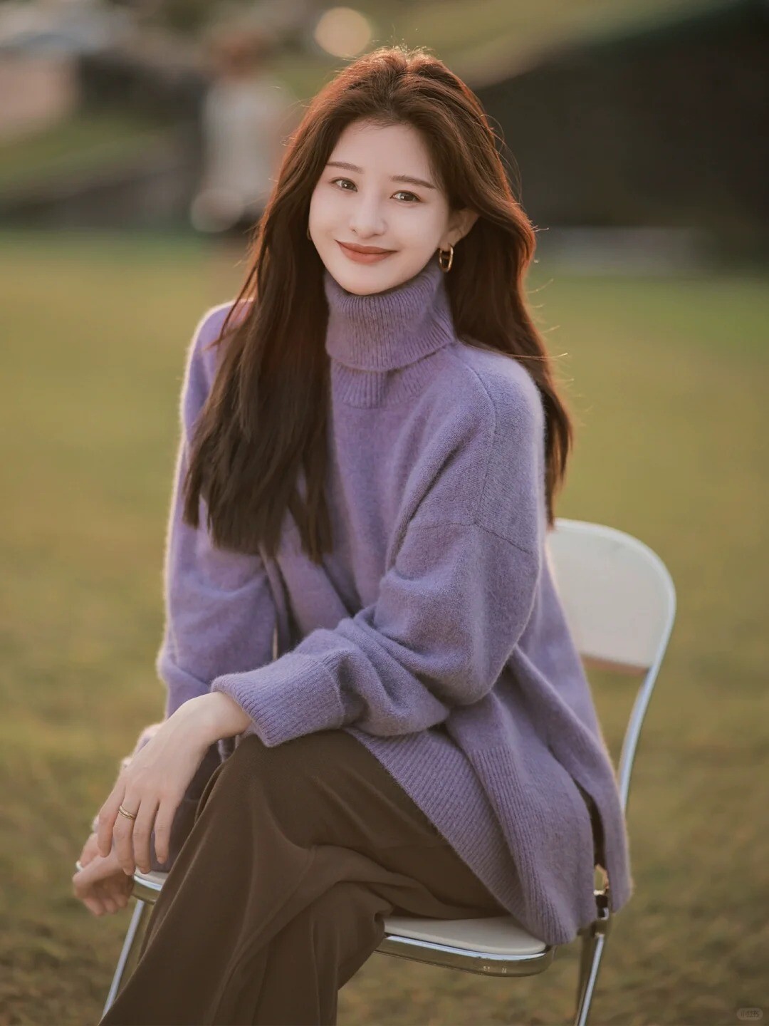 A woman wearing a purple sweater and white pants, posing against a colorful background.