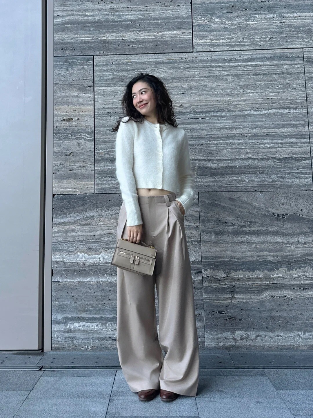 A woman wearing a purple sweater, white pants, and white sneakers, posing against a colorful background.