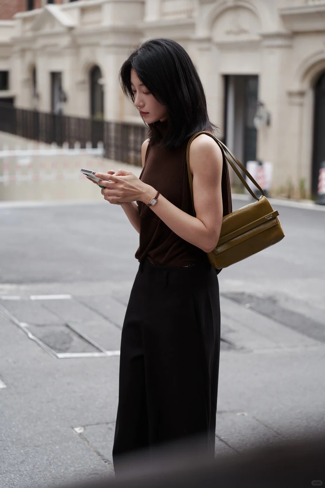 A woman wearing a white sleeveless sweater, white shirt, and blue jeans, posing on a street.