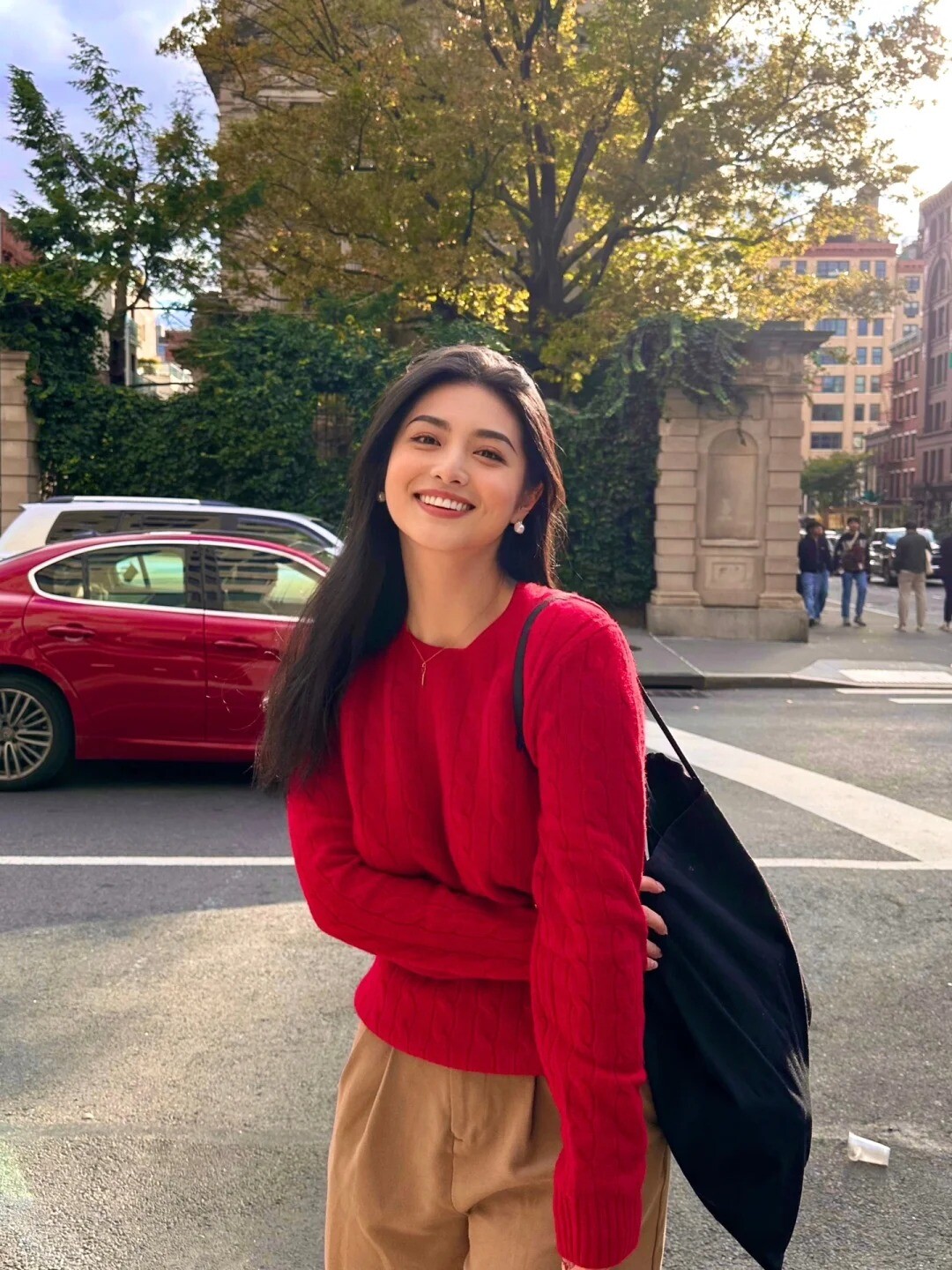 A woman wearing a bright yellow sweater and blue jeans, posing against a colorful mural.