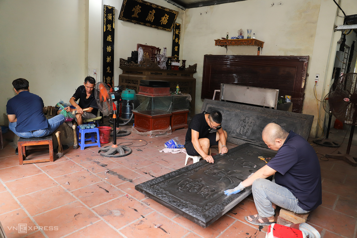9h sáng tại làng Kiêu Kỵ, tiếng búa đã rền vang. Trong xưởng, anh Ninh (áo đen, đeo kính), 27 tuổi, cùng ba người thợ bắt đầu ngày làm việc. Người đập vàng, người chà nhám bề mặt gỗ để chuẩn bị dát (thếp, quỳ) vàng cho một bức hoành phi lớn.
