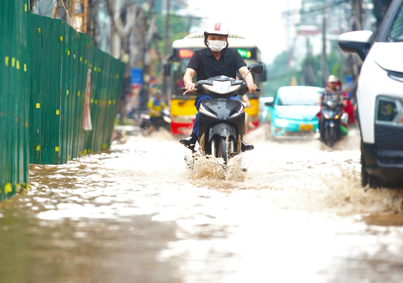 Người điều khiển xe máy co chân băng qua phố ngập nước.