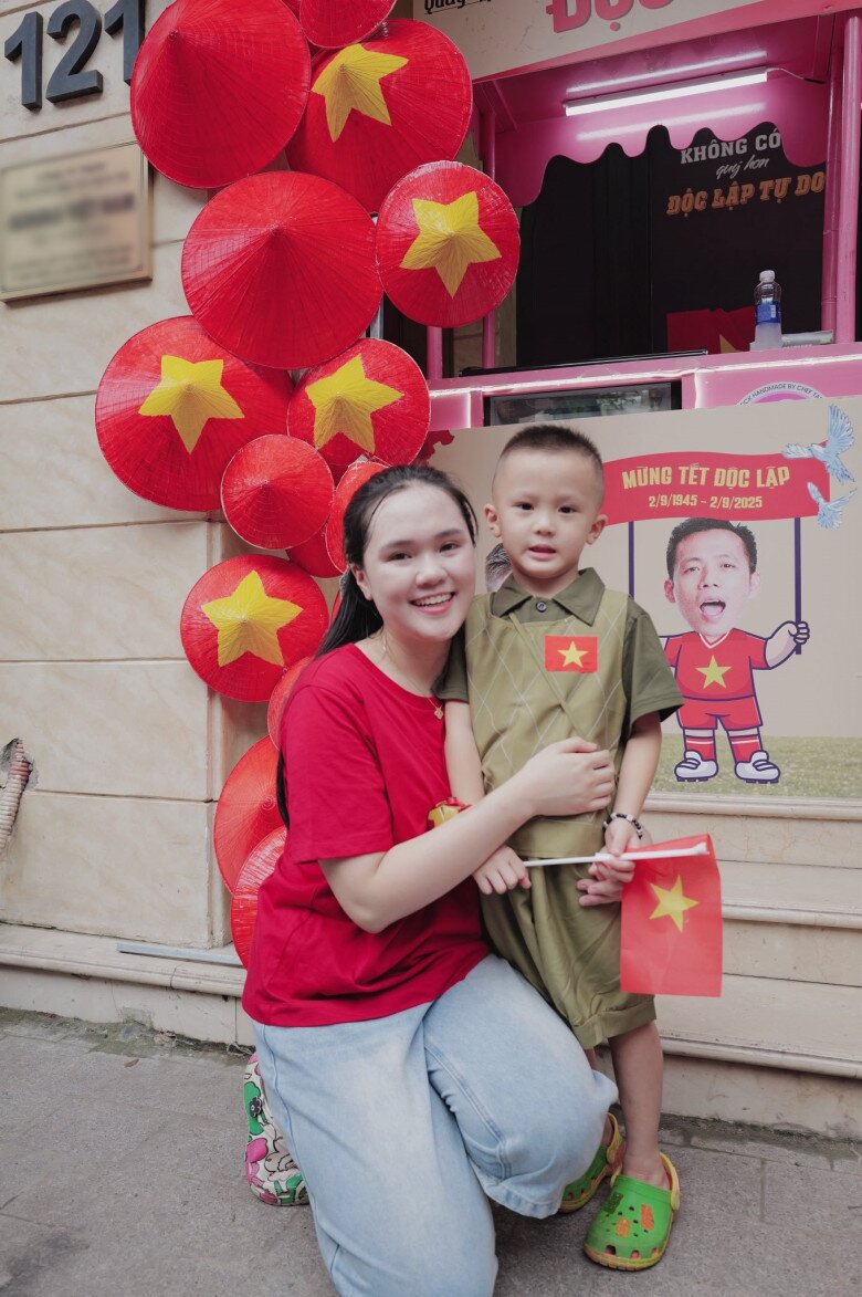 Quỳnh Anh cùng con trai Duy Minh chụp ảnh bên quầy hàng miễn phí của gia đình. Những chiếc nón lá đỏ được sắp xếp theo cụm, xếp dọc từ mặt đất lên cao. Chất liệu mộc mạc nhưng phối hợp hợp lý khiến không gian sinh động mà không rối mắt.