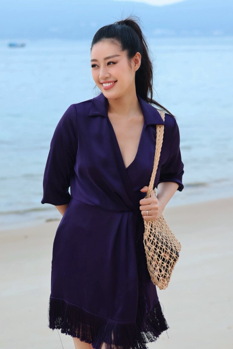 Không cần diện bikini hay trang phục gợi cảm, Khánh Vân vẫn nổi bật giữa khung cảnh biển xanh cát trắng với bộ váy tím đậm đầy thanh lịch. Thiết kế dáng wrap dress (váy quấn) với phần cổ chữ V sâu vừa đủ, tay lỡ nhẹ nhàng và phần tà tua rua tạo hiệu ứng chuyển động uyển chuyển theo từng bước đi.