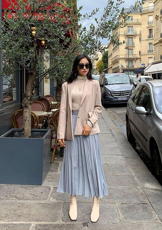 Blazer be phối áo cổ lọ kem và chân váy xếp ly xanh nhạt, tạo tổng thể thanh lịch kiểu Parisian, vừa ấm áp vừa tinh tế cho những ngày thu se lạnh.