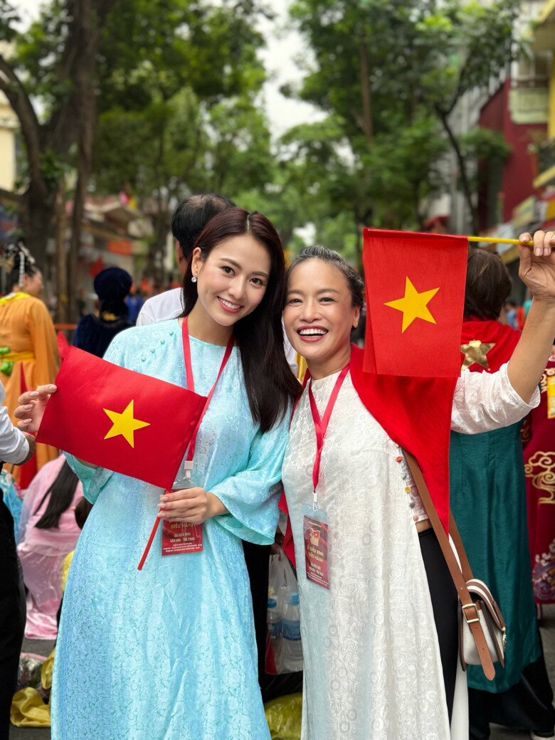 Trong tà áo dài xanh ngọc nhẹ nhàng, diễn viên trẻ Việt Hoa toát lên vẻ thanh thoát, duyên dáng. Kiểu dáng suông mềm mại kết hợp với đôi bông tai nhỏ nhắn càng tôn nét nền nã. Cô diện đồ đồng điệu với mẹ chồng màn ảnh Tú Oanh và cả hai cùng cầm lá cờ đỏ sao vàng, lan tỏa niềm tự hào dân tộc.