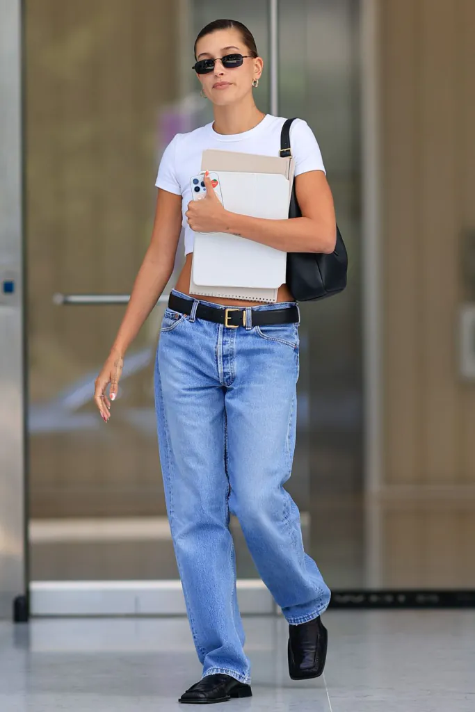 Hailey Bieber một lần nữa xuất hiện trên phố với phong cách đơn giản, lựa chọn áo phông trắng ngắn cùng quần jeans cạp trễ, kết hợp thắt lưng da đen, giày lười mang đến vẻ ngoài gọn gàng, sạch sẽ thường ngày.
