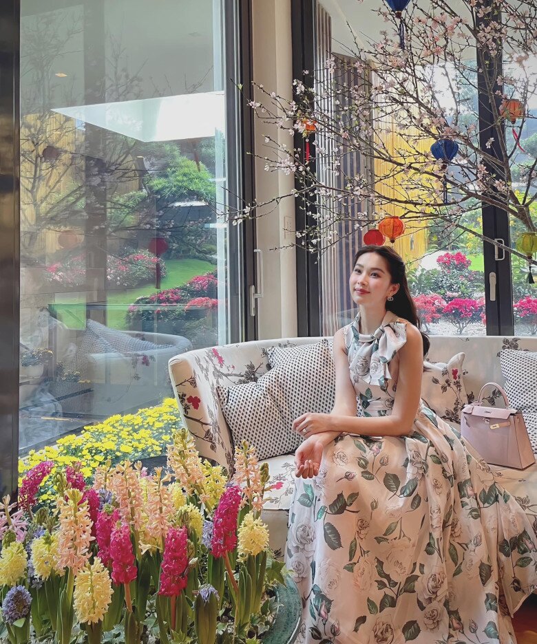 Váy maxi hoa hồng nhã nhặn với điểm nhấn là nơ lớn ở cổ tạo nên vẻ thanh lịch, đài các. Dáng váy xòe nhẹ giúp che bụng khéo léo, phần tay sát nách ôm gọn vừa phải – đủ để khoe vai thon mà không lộ nhược điểm.