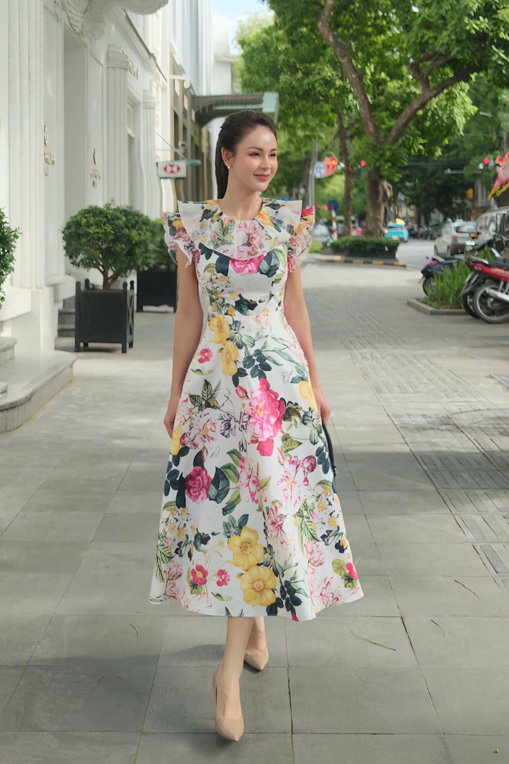 Váy midi họa tiết hoa nổi bật trên nền trắng với phần vai bèo cách điệu. Thiết kế cổ vuông + chiết eo nhẹ tôn dáng nhưng vẫn kín đáo. Tay áo phủ kín bắp tay, phần chân váy xòe che bụng tài tình – hoàn hảo cho phong cách quý cô thanh lịch tuổi U40.