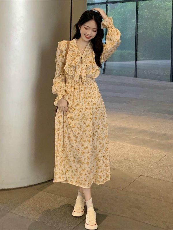 Váy hoa vàng tay dài, cổ nơ mang phong cách tiểu thư lãng mạn. Dáng váy dài qua gối, chất liệu mỏng nhẹ giúp thoáng mát.