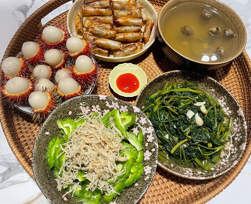 Một mâm cơm đậm đà hương vị với rau muống xào tỏi thơm nồng, mướp đắng ruốc thịt bùi ngậy, thêm ram tôm đất giòn rụm. Bát canh rau muống dầm sấu chua mát cùng đĩa chôm chôm tráng miệng làm bữa ăn càng thêm dễ chịu.
(Ảnh: Hòa Bùi)