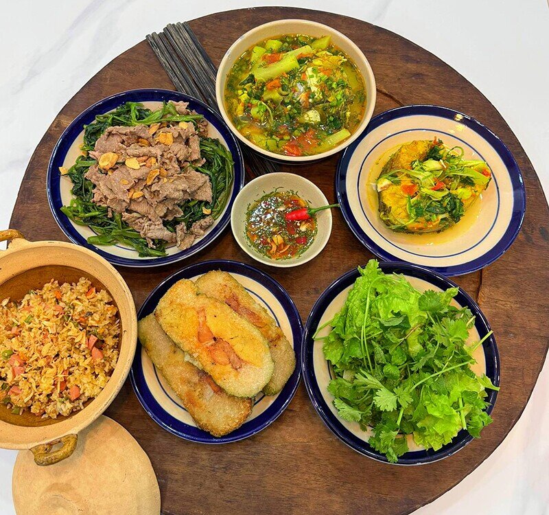 Một mâm cơm mang hơi thở quen thuộc với canh chua cá chua ngọt hài hòa, bò xào rau muống đậm đà, thêm đĩa cơm rang vàng óng. Rau sống ăn kèm tăng vị tươi mát cùng bánh chưng rán thơm nức.
(Ảnh: Tâm Nguyễn)