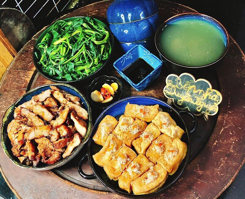 Một mâm cơm dung dị nhưng đưa đẩy vị giác với nọng heo sá xíu mềm ngọt, đậu phụ chiên tẩm mắm ruốc đậm đà, đĩa rau muống luộc xanh mướt cùng bát canh rau muống dầm sấu chua thanh, đủ làm bữa ăn thêm trọn vẹn. (Ảnh: Thùy Duyên Nguyễn)