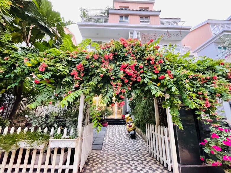 Cổng nhà phủ đầy hoa giấy và dây leo tạo thành vòm hoa rực rỡ, lối vào lát gạch họa tiết tròn giản dị nhưng sạch sẽ, gợi cảm giác mộc mạc, gần gũi như một ngôi nhà miền quê thu nhỏ giữa lòng phố.