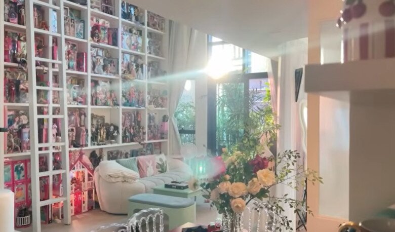 Tường phòng khách biến thành “bảo tàng Barbie” với hệ kệ cao kịch trần chứa hàng trăm búp bê đủ phong cách. Ghế sofa bo tròn và nội thất pastel tạo cảm giác mềm mại, nữ tính.