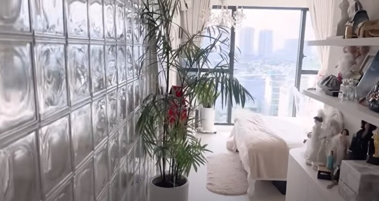 Lối đi vào phòng ngủ là bức tường kính lấy sáng, nổi bật với cây xanh lớn như một điểm nhấn thiên nhiên. Không gian tinh giản nhưng vẫn giữ nét duyên nhờ các món trang trí gợi cảm hứng cổ tích.