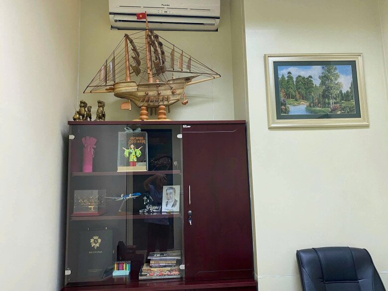 Một góc phòng được sắp xếp thành khu vực làm việc và lưu niệm, với tủ gỗ kính đựng các món đồ cá nhân như ảnh cô Đẩu Công Lý, mô hình, sách, cúp lưu niệm và các vật phẩm trưng bày.