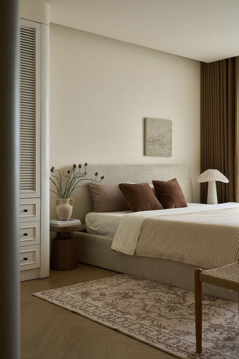 Phòng ngủ master ấm áp và yên bình. Giường bọc vải tông beige kết hợp gối nâu đất, tạo cảm giác êm ái, dễ chịu. Hệ rèm dày, thảm trải sàn và đèn ngủ cùng tông góp phần tạo nên sự đồng bộ.