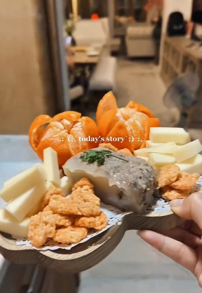 Trên chiếc khay gỗ hình trái tim, ông xã đại gia chuẩn bị khéo léo một phần ăn nhẹ gồm: Pate thịt nấu đông, phô mai cắt que, bánh phồng tôm chiên giòn, quýt bóc vỏ tỉ mỉ và baguette Pháp giòn tan.