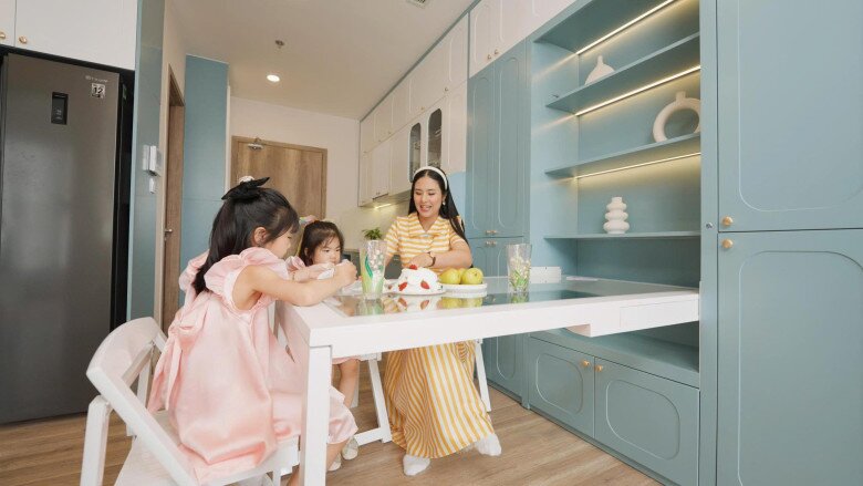 Bếp nhỏ gọn cùng tông màu xanh dịu. Chiếc bàn ăn nếu hất lên sẽ thành cánh cửa cho chiếc kệ trang trí, ngả xuống là 3 bác cháu có chỗ tha hồ vẽ tranh.
