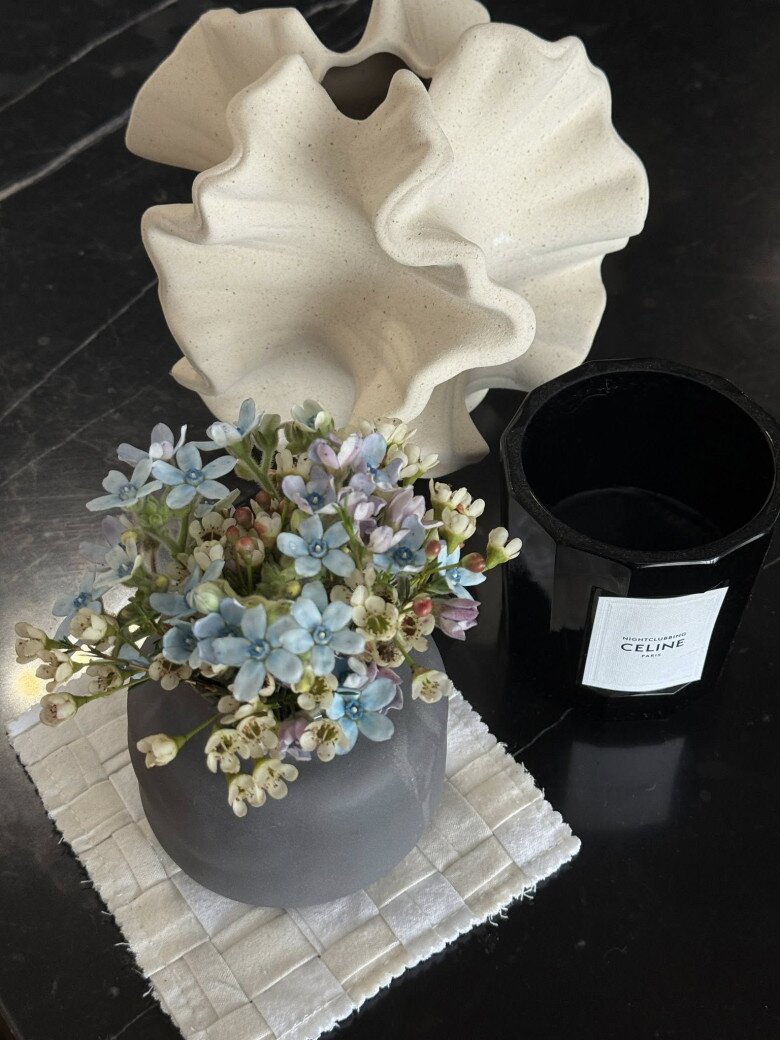 Hoa lam tinh tông pastel được nam stylist cắm trong bình gốm xám mờ, đặt cạnh nến và bình điêu khắc gốm lạ mắt. Tổ hợp nhẹ nhàng, phù hợp với phong cách tối giản và hơi hướng nghệ thuật.