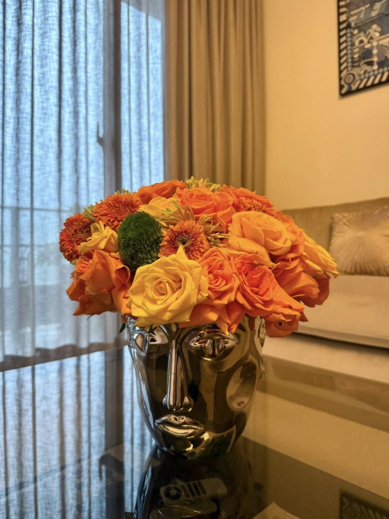 Lọ đầu tượng chrome bạc tạo điểm nhấn hiện đại, phối hoa cam – vàng nổi bật. Cách cắm bo tròn giúp tôn hình khối của bình, tạo hiệu ứng “mũ hoa” độc đáo.