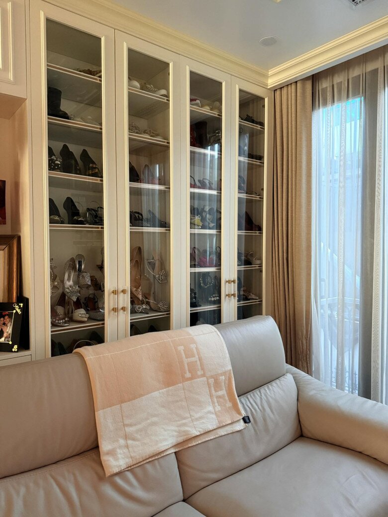 Một mảng tường lớn được tận dụng làm tủ trưng bày giày và phụ kiện. Cửa kính trong suốt giúp căn phòng thoáng hơn, vừa khéo khoe được gu thời trang của gia chủ. Ghế sofa da tone beige cùng khăn hàng hiệu tạo cảm giác thư giãn nhưng không kém phần đẳng cấp.