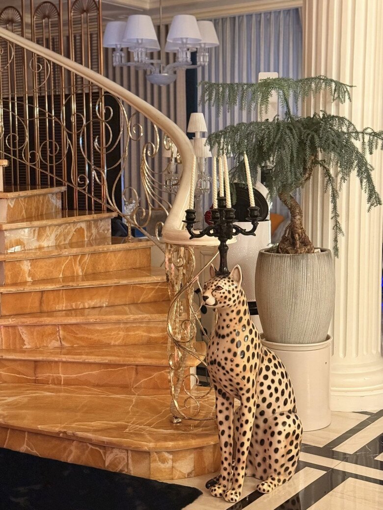 Cầu thang được ốp đá marble vàng vân nổi bật, tay vịn uốn lượn ánh kim, đi cùng đèn tường cổ điển và tượng mèo Bengal gốm đứng canh gác ở chiếu nghỉ. Chính chi tiết này khiến dân mạng chú ý, nhưng cũng là điểm nhấn cá tính của chủ nhân ngôi nhà.