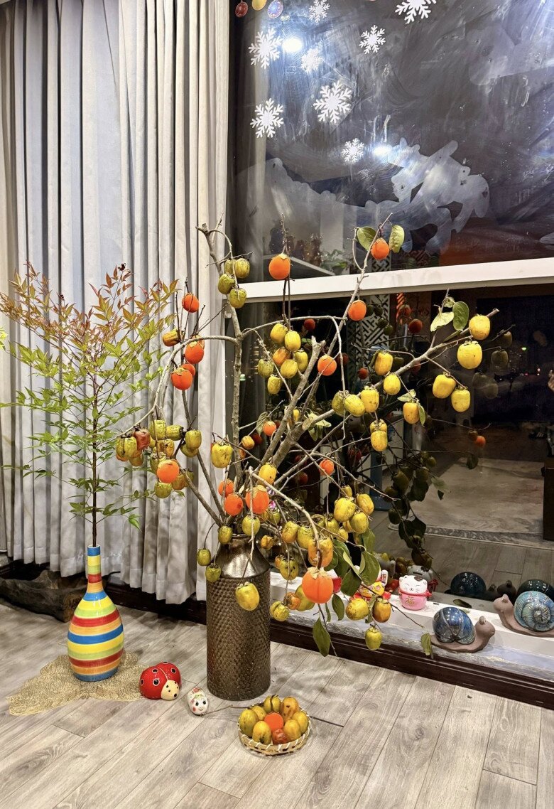 Trái hồng đã bắt đầu chuyển đỏ xen lẫn trái còn vàng, tạo hiệu ứng thị giác rất bắt mắt. Bên cạnh là chậu cây cảnh nhỏ và bình gốm sọc nhiều màu, góp phần hoàn thiện một không gian rất mùa thu.