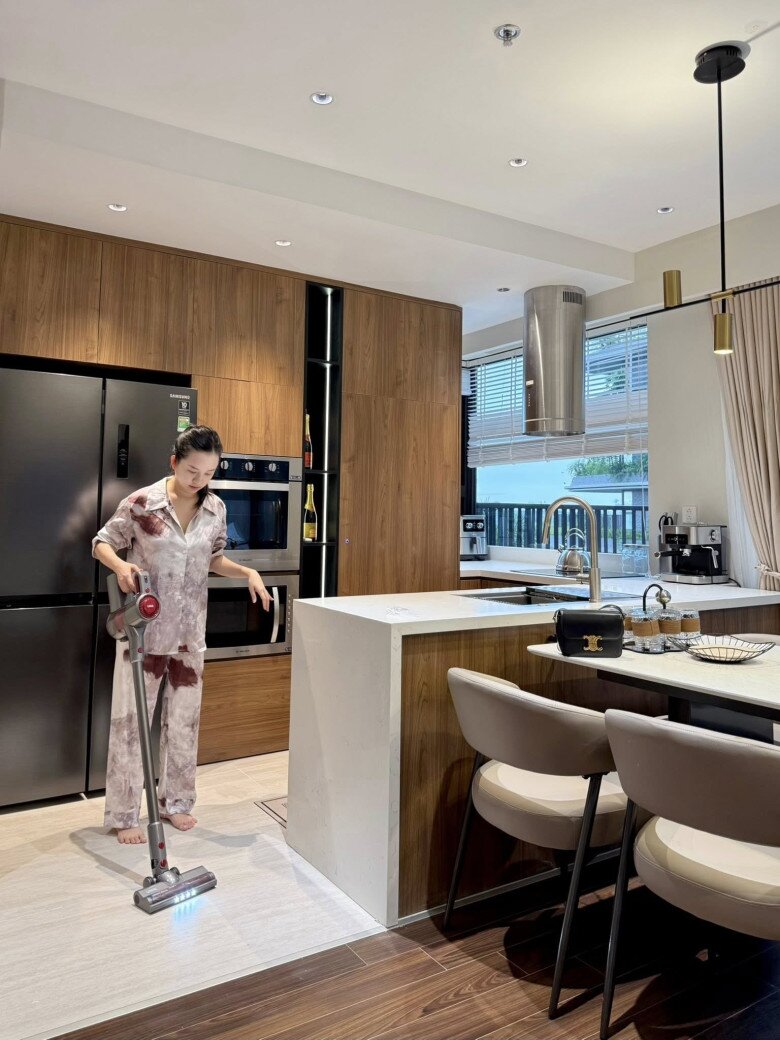 Ly Kute dọn dẹp khu bếp. Khu vực bếp là trái tim của căn nhà, đúng như chia sẻ của nữ diễn viên. Tủ bếp gỗ ấm áp, thiết kế âm tường gọn gàng, kết hợp bàn đảo tiện nghi.