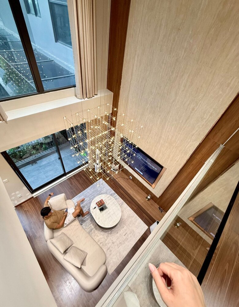 Căn hộ mới nhất tiếp tục ghi dấu phong cách sống hiện đại, tối giản nhưng đầy cảm xúc. Đây là một căn hộ thông tầng được thiết kế hiện đại. Góc nhìn từ trên cao cho thấy thiết kế trần cao ấn tượng cùng đèn thả ánh vàng hiện đại tạo điểm nhấn.