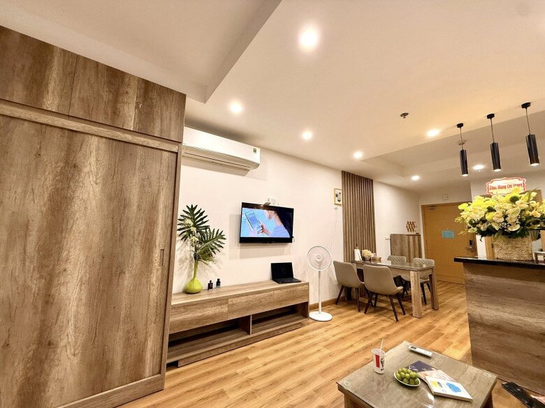 Nhìn từ góc này, tổng thể phòng khách - bếp - bàn ăn được bố trí thông minh trên nền sàn gỗ sáng, vừa gọn gàng vừa chan hòa ánh sáng đèn ấm cúng. Một không gian đủ đầy để cả gia đình quây quần.