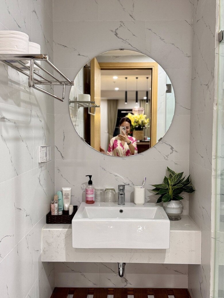 Phòng tắm nhỏ xinh với gương tròn tối giản, bồn rửa hiện đại và đầy đủ đồ dùng cá nhân. Một chậu cây xanh giúp góc vệ sinh trở nên sinh động và tươi mát hơn.