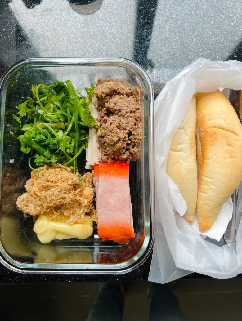 Bữa bánh mì “5 topping” với chả, pate, ruốc, xíu mại, sốt mayonnaise và rau thơm. Bên cạnh là hai ổ bánh mì - bữa ăn nhẹ nhàng mà vẫn đủ chất và ngon lành.
