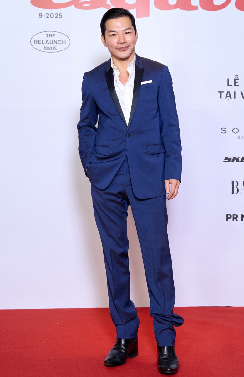 Nam diễn viên – doanh nhân Trần Bảo Sơn chọn bộ suit xanh navy điểm ve áo satin đen, phối cùng sơ mi trắng cổ mở. Phong cách tối giản nhưng tinh tế, vừa tôn lên vóc dáng vừa tạo cảm giác tự tin, phong độ. Đôi giày da đen cổ điển hoàn thiện hình ảnh “quý ông lịch lãm” quen thuộc của anh trên thảm đỏ.