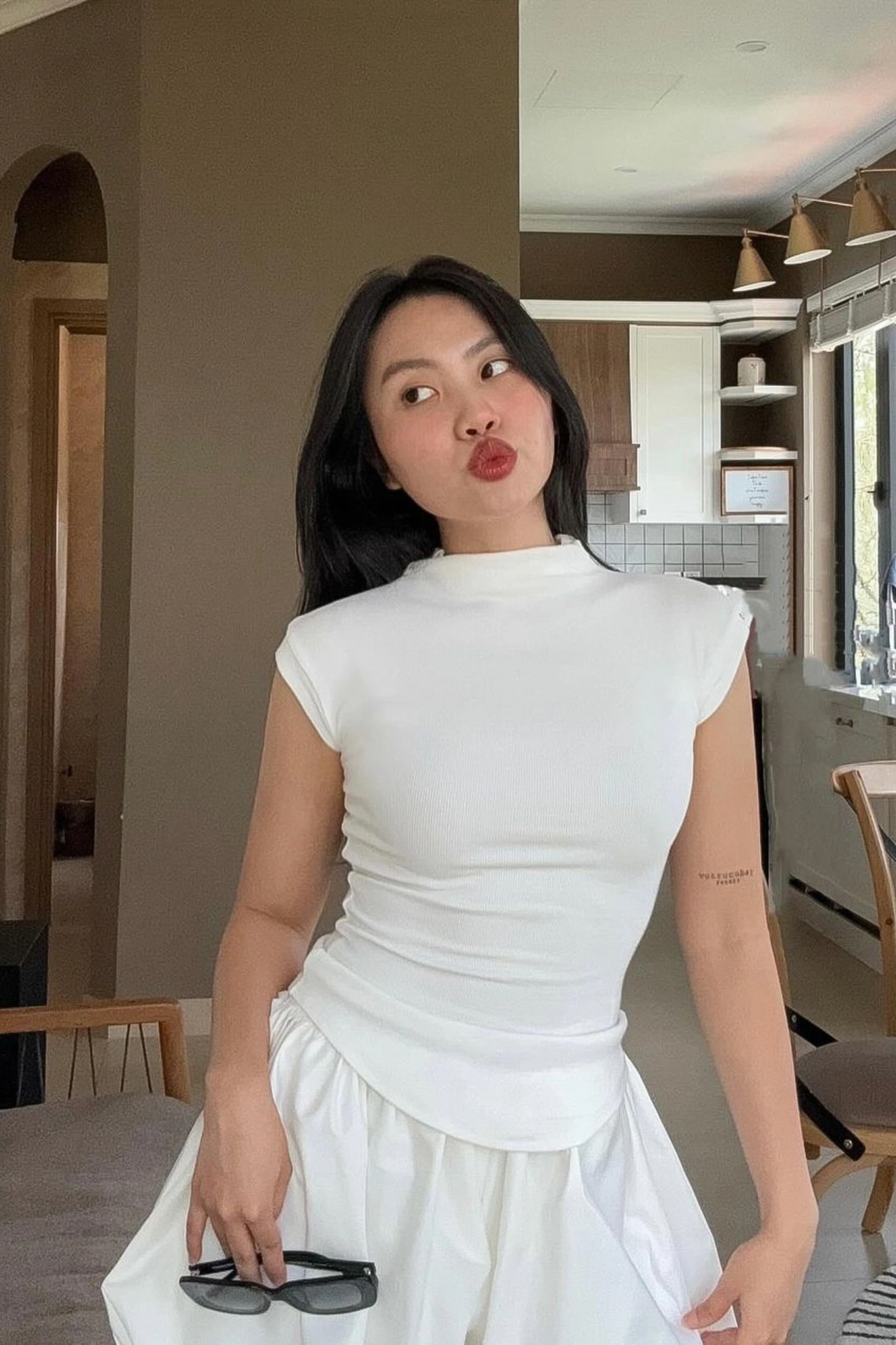 Trong một bức hình đời thường, Phương Mỹ Chi diện áo thun ôm sát tay ngắn kết hợp chân váy xếp ly trắng, toát lên vẻ đẹp nhẹ nhàng, tối giản nhưng vẫn thu hút nhờ kiểu dáng tôn dáng và sự chỉn chu trong lựa chọn phụ kiện như kính râm cầm tay. Đây là phong cách phù hợp với hình ảnh một cô gái Gen Z trưởng thành nhưng vẫn giữ nét ngây thơ trong sáng.