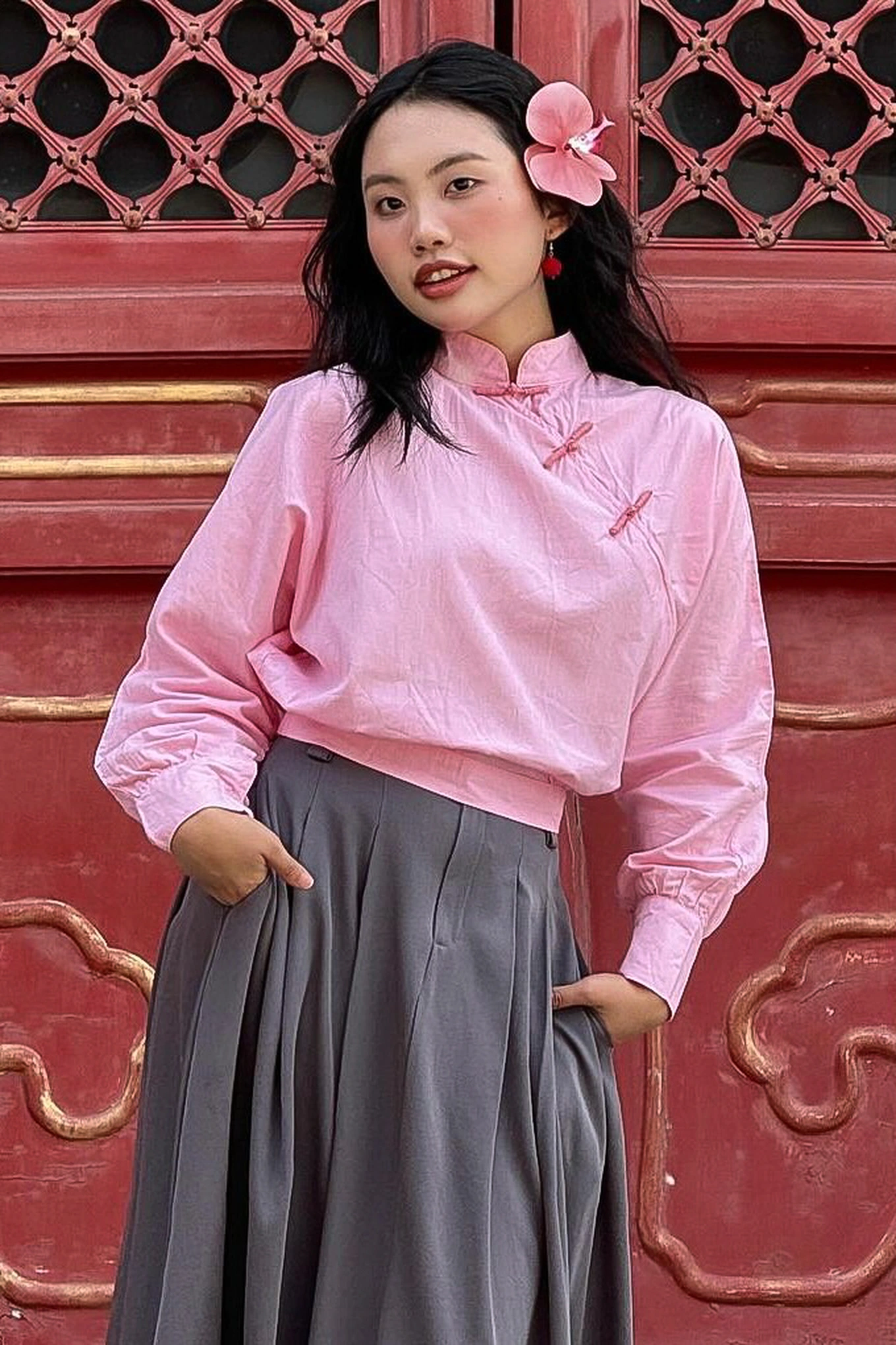 Một hình ảnh rất đáng yêu của Mỹ Chi là khi cô diện áo tay dài cổ tàu hồng pastel phối cùng chân váy xếp ly xám, tóc thả nhẹ điểm xuyến hoa tai và hoa cài đầu. Set đồ gợi cảm hứng từ phong cách Hán phục hoặc thời trang cổ trang nhẹ nhàng, vừa duyên dáng vừa độc đáo. Đây là một cách rất thông minh để cô nàng thể hiện tình yêu văn hóa truyền thống theo cách riêng biệt.