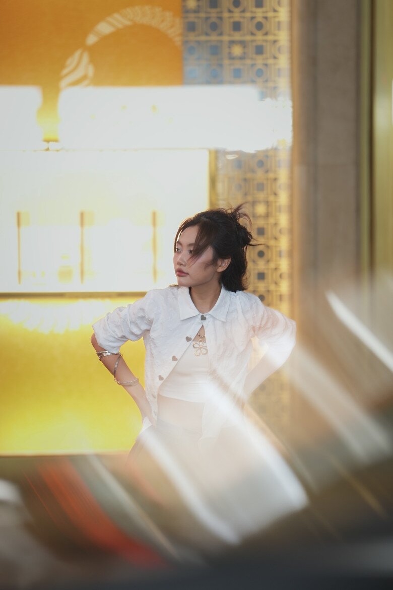 Trong ánh sáng rực rỡ của đô thị về đêm, Phương Mỹ Chi xuất hiện với áo khoác trắng thêu họa tiết trái tim, áo thun croptop phối bralette bên trong. Kiểu tóc búi cao phóng khoáng và biểu cảm lạnh lùng làm tăng vẻ chất chơi và hiện đại. Đây là hình ảnh hoàn toàn mới mẻ, thể hiện bản lĩnh thử nghiệm của cô với thời trang.