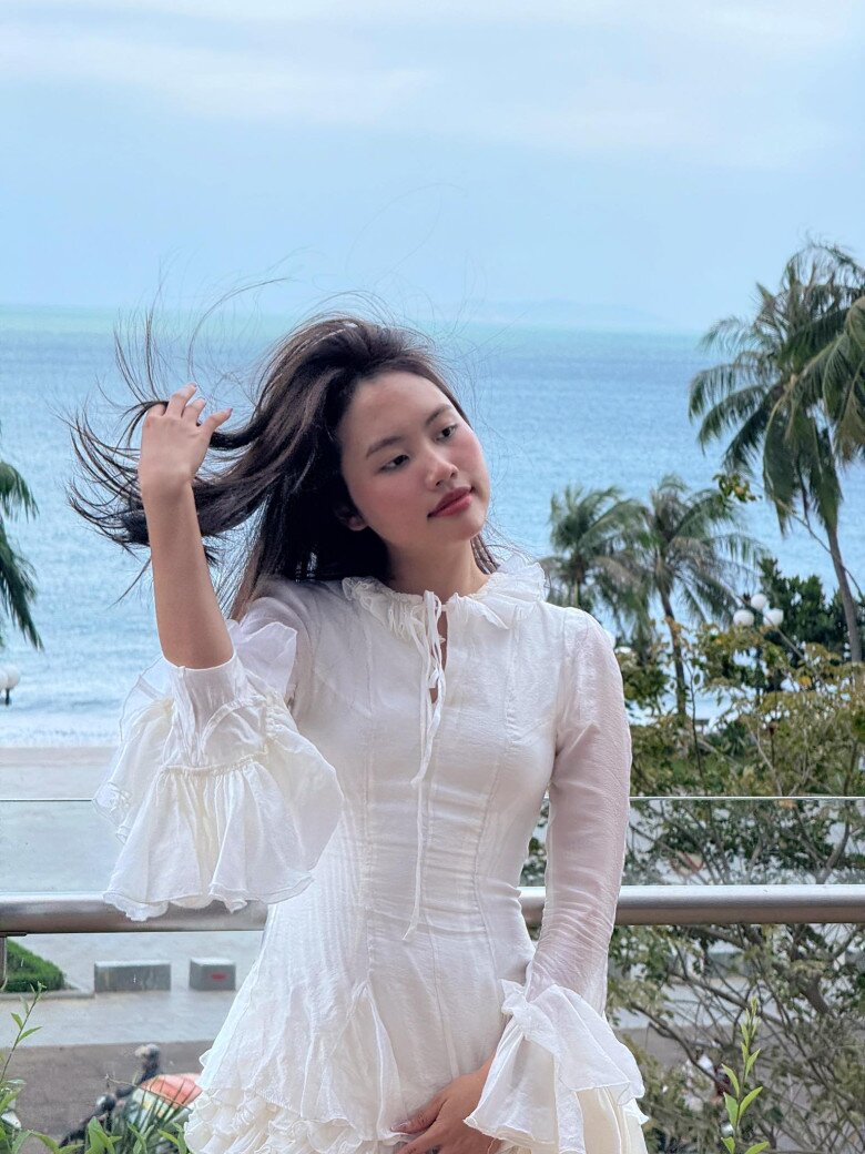 Chiếc váy trắng bo eo, tay loe và phần cổ xếp bèo giúp Mỹ Chi trở nên như nàng thơ giữa khung cảnh biển xanh. Cô toát lên vẻ lãng mạn, cổ điển nhưng vẫn quyến rũ, đúng với tinh thần của các bộ ảnh resort cao cấp.