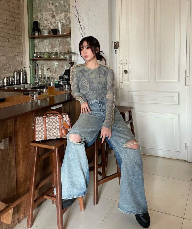 Min diện áo xuyên thấu body-hugging với họa tiết mờ ảo, phối cùng quần jeans ống rộng rách gối đầy chất chơi. Outfit này ghi điểm bởi sự cân bằng giữa quyến rũ (áo ôm, hơi xuyên thấu) và street style bụi bặm (quần jeans phá cách). Chiếc túi họa tiết cổ điển giúp tạo điểm nhấn thời thượng và “giàu vibe” vintage.