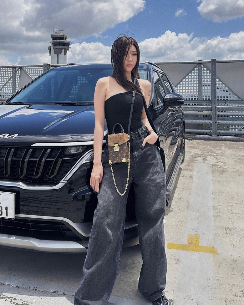 Trên nền trời và background bãi đậu xe cực “cool”, Min lựa chọn áo croptop lệch vai đen tuyền kết hợp với quần jeans ống rộng cạp cao. Cách phối này làm nổi bật vòng eo thon gọn cùng vẻ ngoài sắc sảo. Chiếc túi Louis Vuitton mini đeo chéo là điểm nhấn đắt giá, khẳng định gu thời trang “sành điệu nhưng không phô trương”.
