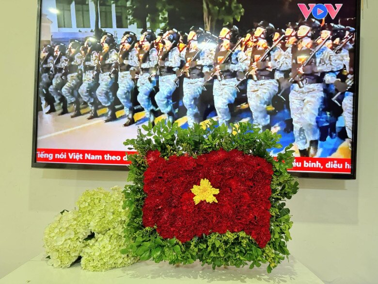 Một lá cờ Tổ quốc được kết từ hoa tươi do chị Ngô Trà Giang tạo nên. Nền đỏ bằng hoa cẩm chướng, ngôi sao vàng rực bằng hoa cúc nổi bật một góc nhà. Tác phẩm này đặt phía trước màn hình đang phát hình ảnh duyệt binh trang nghiêm. Sự kết hợp giữa sắc hoa và hình ảnh người lính tạo nên không khí thiêng liêng, hào hùng chào mừng Quốc khánh 2/9, thể hiện tình yêu nước một cách tinh tế và đầy cảm xúc.