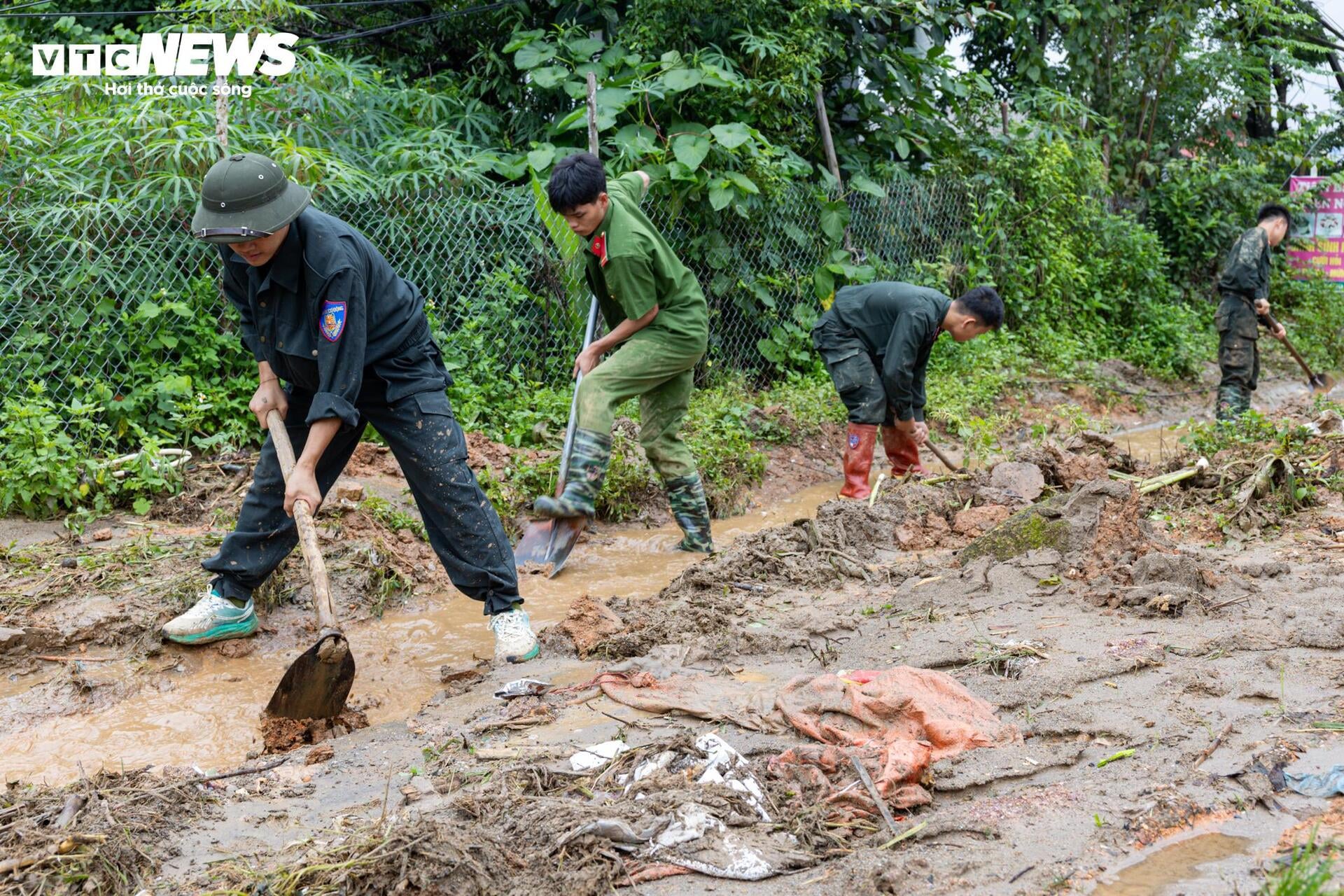 Giữa bùn đất ngổn ngang, hàng chục cán bộ, chiến sĩ công an, quân đội miệt mài giúp người dân dọn dẹp, khắc phục hậu quả lũ quét.