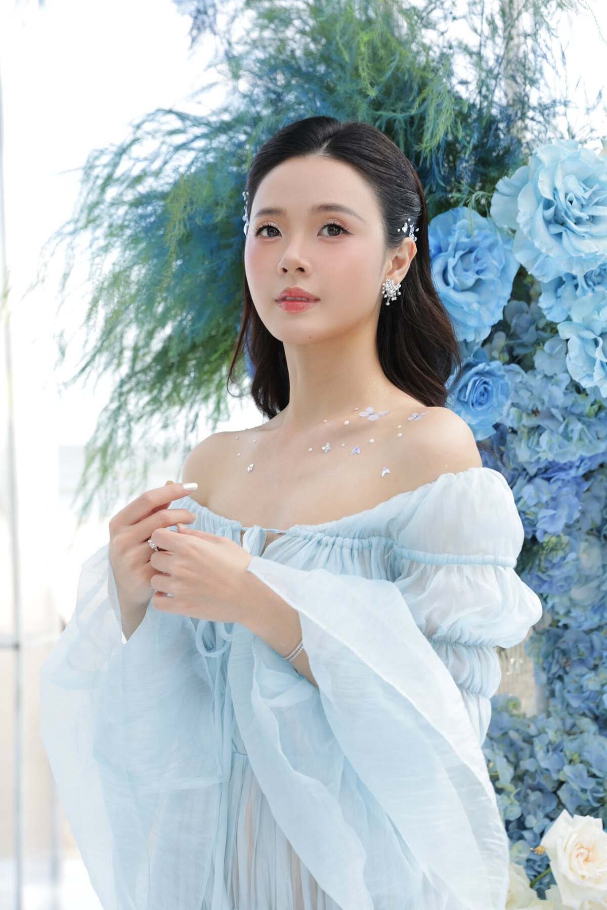Người đẹp sử dụng thêm phụ kiện cài tóc hình cánh bướm, hoa tai đính đá. Việc gắn các hạt pha lê nhỏ trên vai giúp tổng thể có thêm điểm nhấn.