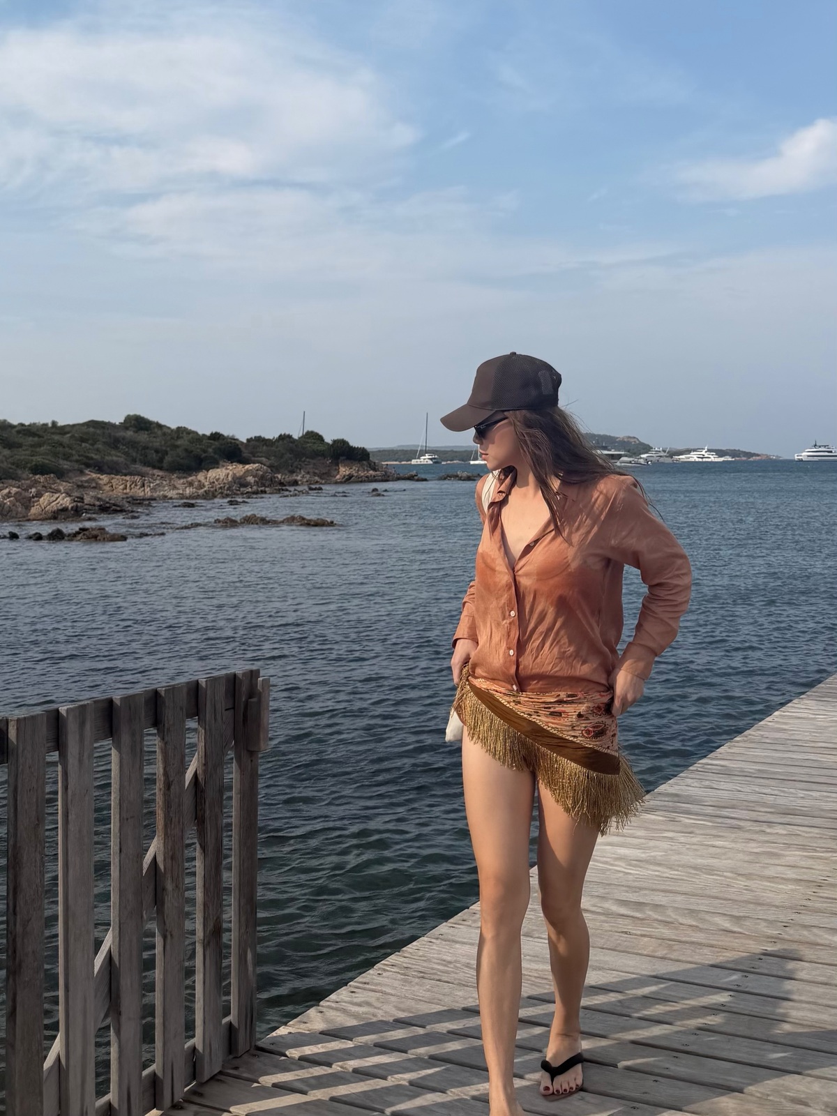 Bà mẹ ba con diện sơ mi trễ nải bên ngoài bikini, phối cùng khăn quấn tua rua đồng điệu gam nâu khi ngắm biển ở Italy.
